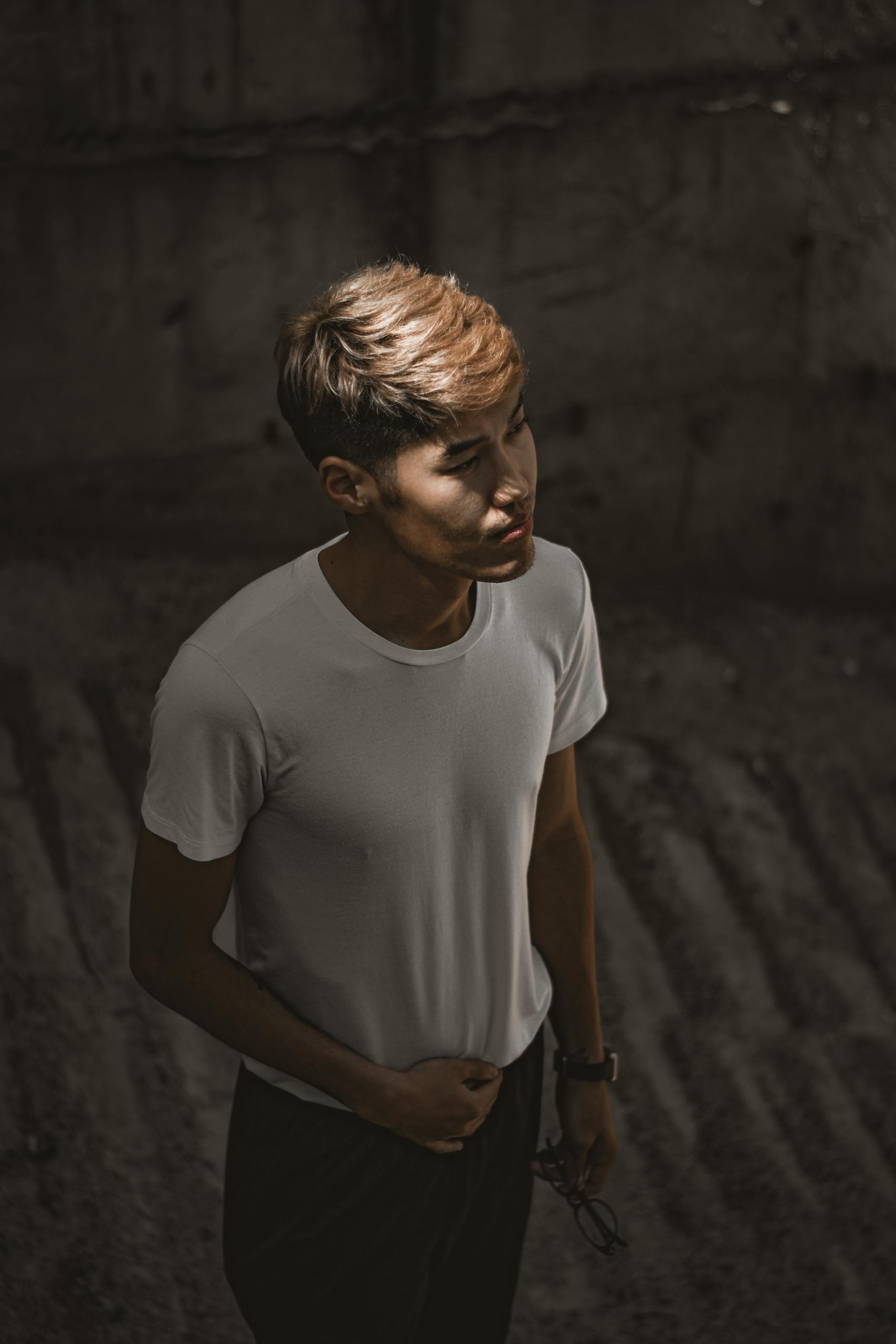 An introspective young man stands in moody lighting, creating a dramatic effect.