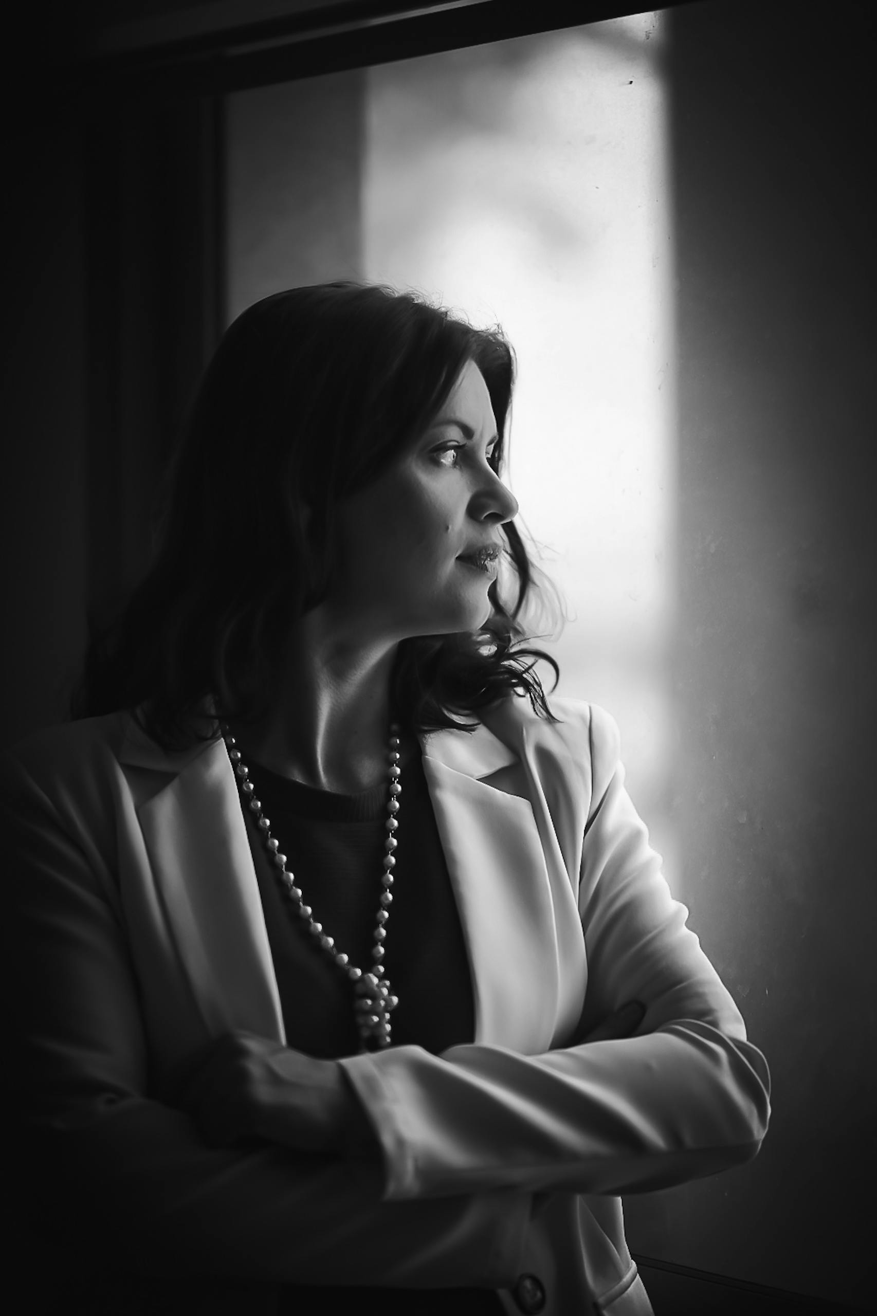 Black and white portrait of an elegant woman looking contemplatively out a window.
